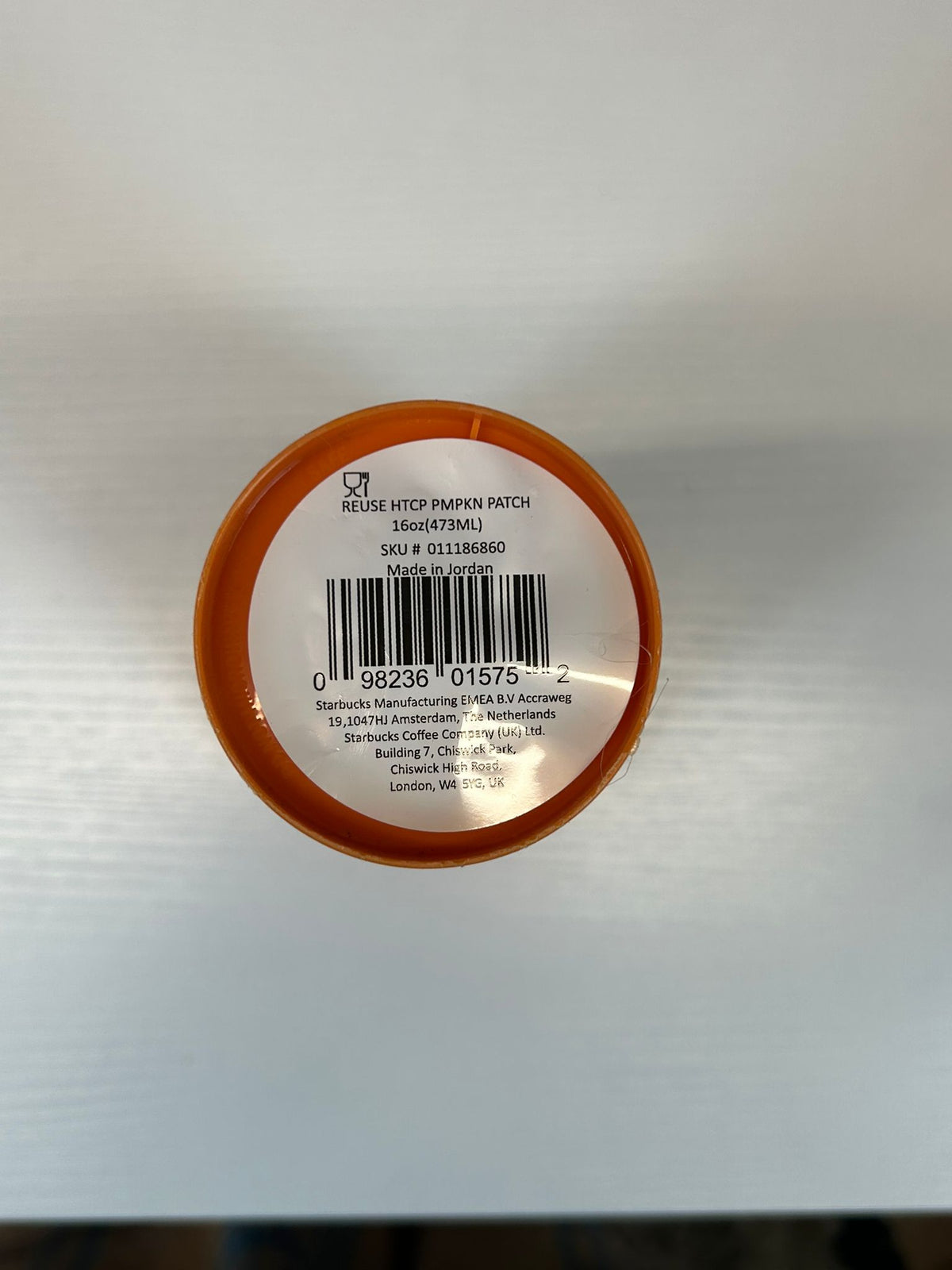 Top-down view of a round orange-lidded container showing a white barcode label with product text and a barcode .